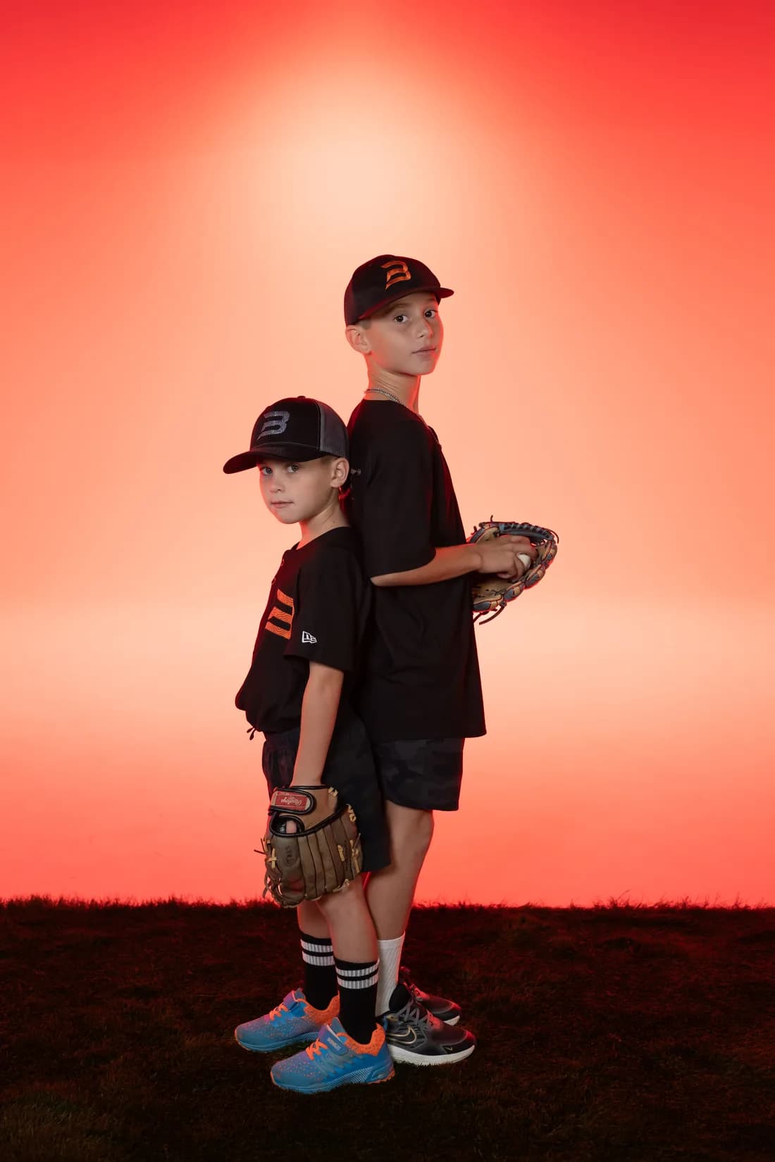 Trés and Bronco Lundin standing back to back in ONBASE Athlete caps and tees, gloves in hand, against a red studio backdrop